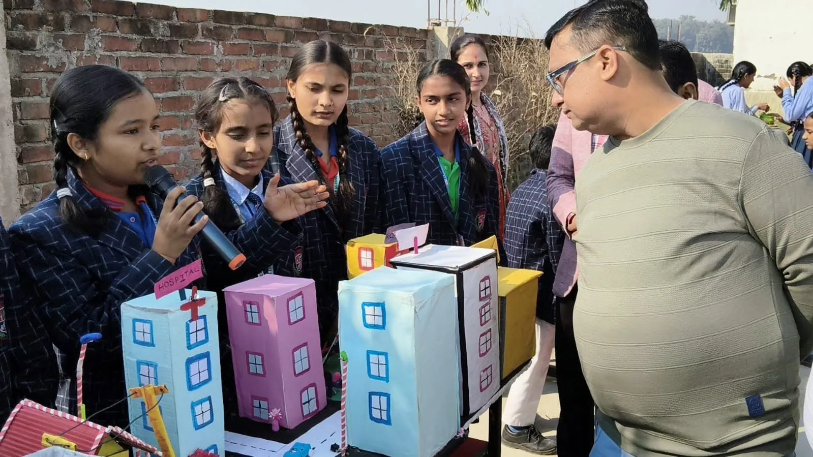 Students standing beside hand-built model houses at the school exhibition